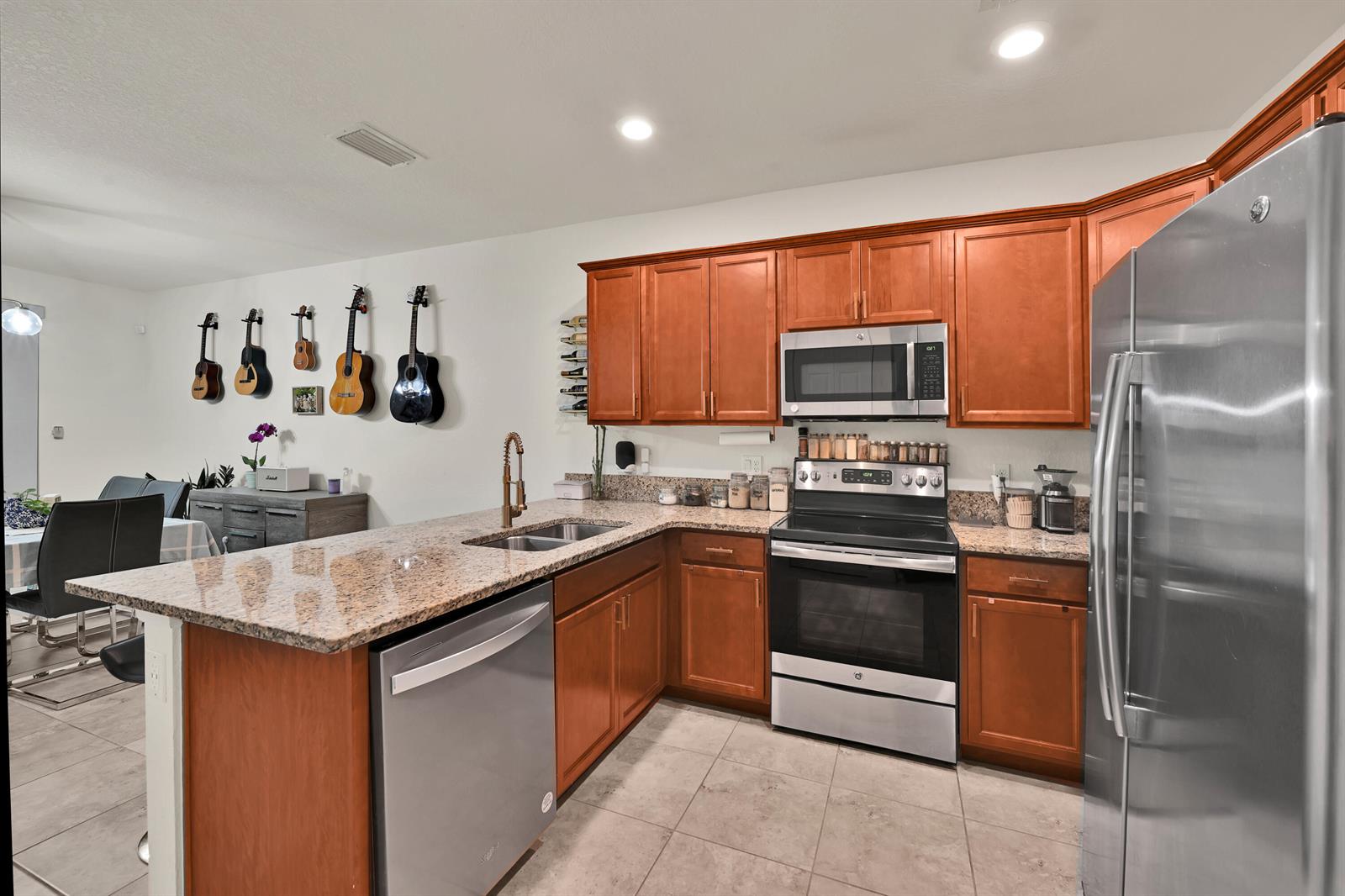 A kitchen features wood cabinets, granite countertops, stainless steel appliances, and a wall of guitars — 6977 Broadland Way, Coconut Creek FL 33073, COCONUT CREEK, FL