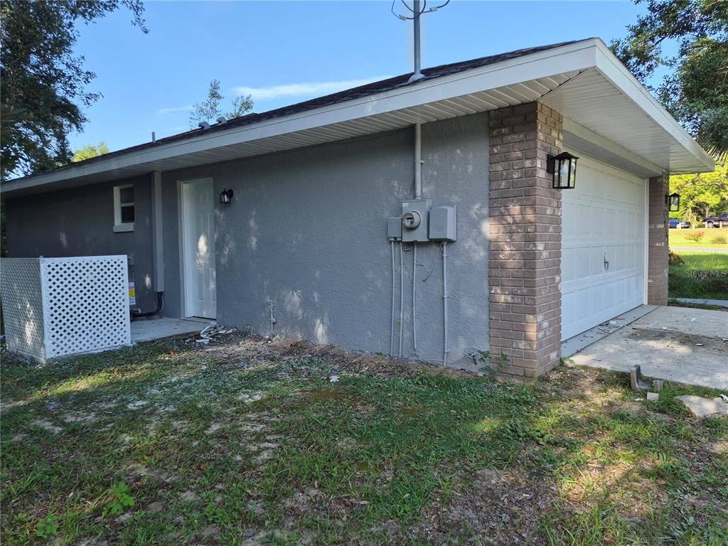 The exterior side of a house features a gray stucco wall, a garage door, and a door — 1213 W SORRENTO DRIVE, CITRUS SPRINGS, FL