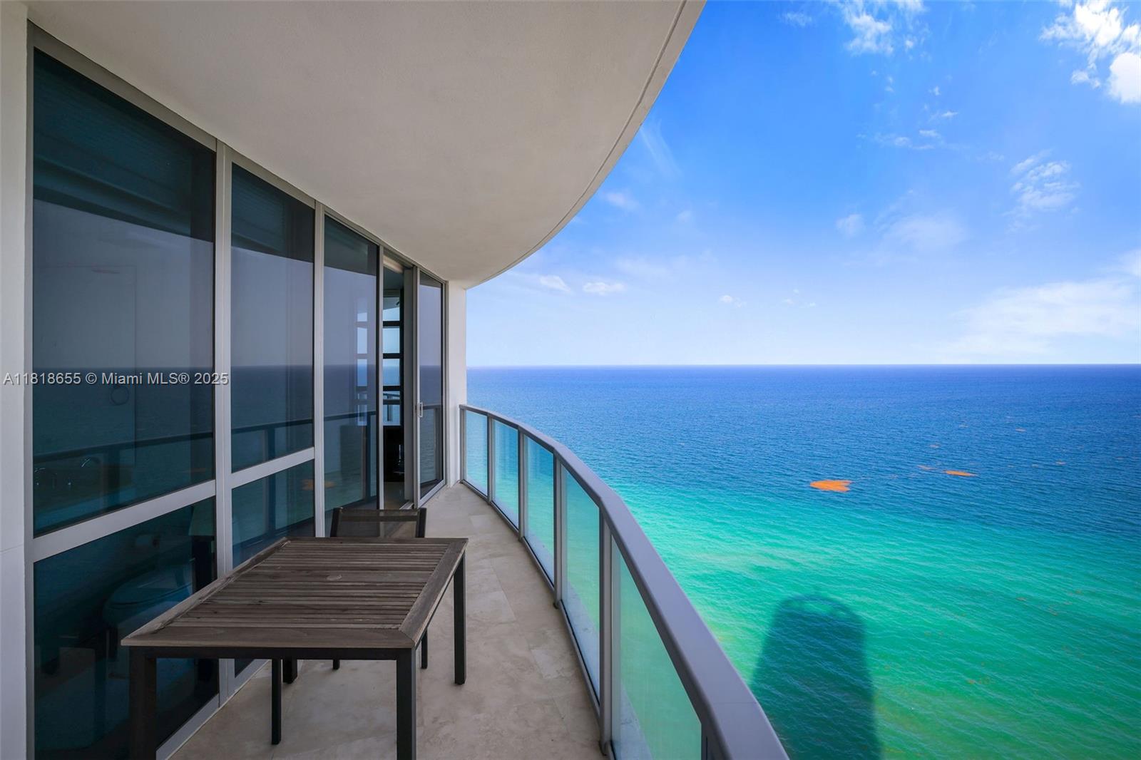 A curved balcony with a wooden table overlooks the ocean under a clear blue sky — 3101 S Ocean Dr # 2708, Hollywood FL 33019, HOLLYWOOD, FL
