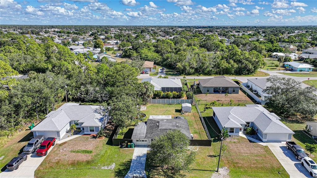 An aerial view shows three suburban houses with driveways and surrounding trees under a blue sky — 819 HALEYBURY STREET NW, PORT CHARLOTTE, FL
