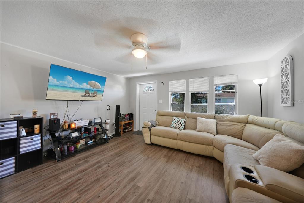 A living room features light wood-look flooring, a beige sectional sofa, and a wall-mounted television — 819 HALEYBURY STREET NW, PORT CHARLOTTE, FL