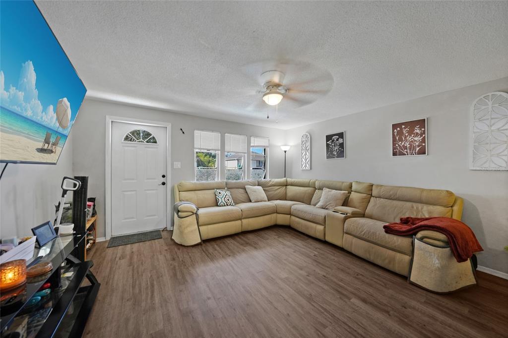 A living room features light-colored walls, wood-look flooring, a large sectional sofa, and a television — 819 HALEYBURY STREET NW, PORT CHARLOTTE, FL