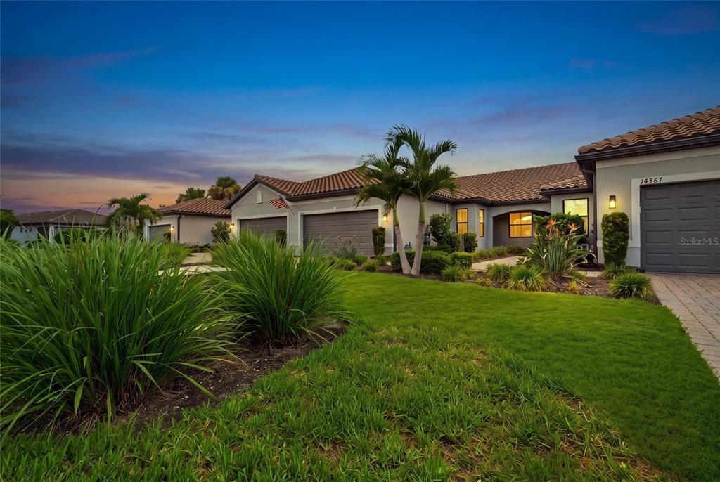 A single-story house with a tile roof, three-car garage, and landscaped lawn at sunset — 14571 MOSSY PINE COURT, NOKOMIS, FL