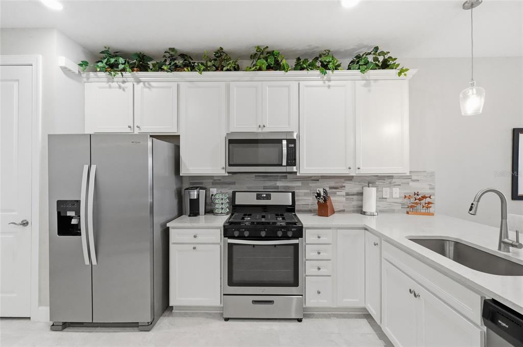 A kitchen with white cabinets, stainless steel appliances, a tiled backsplash, and artificial greenery above — 14571 MOSSY PINE COURT, NOKOMIS, FL