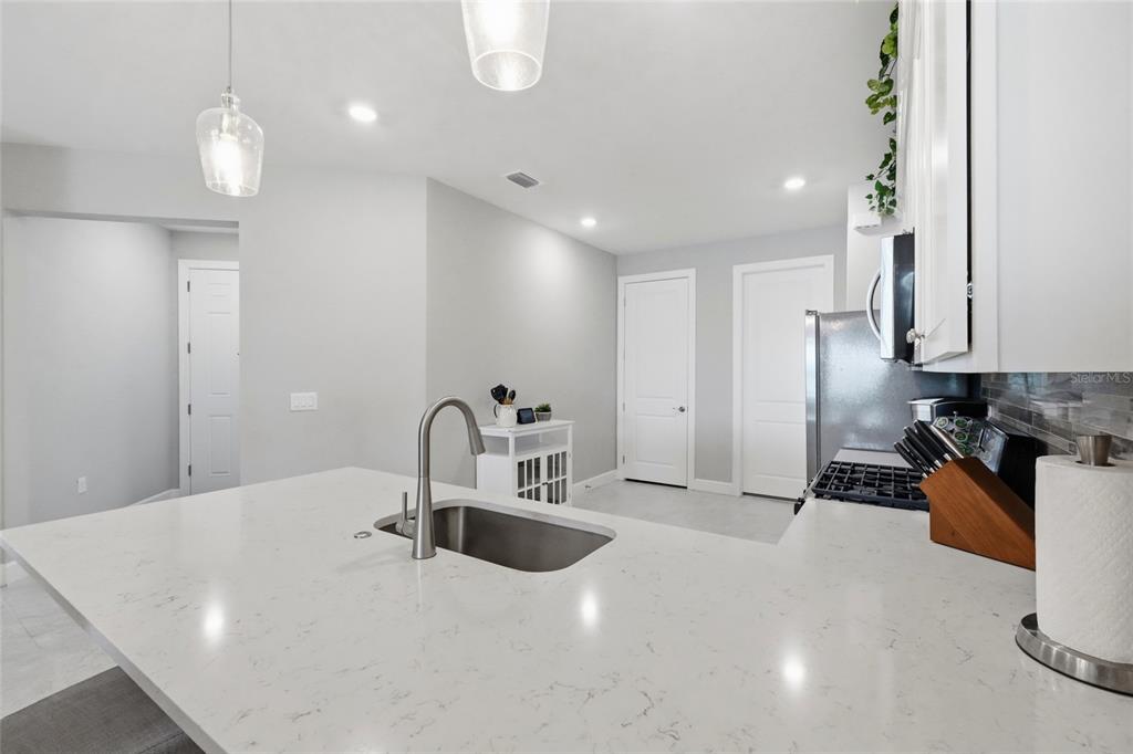 A kitchen features a white quartz island with a sink, stainless appliances, and white cabinetry — 14571 MOSSY PINE COURT, NOKOMIS, FL