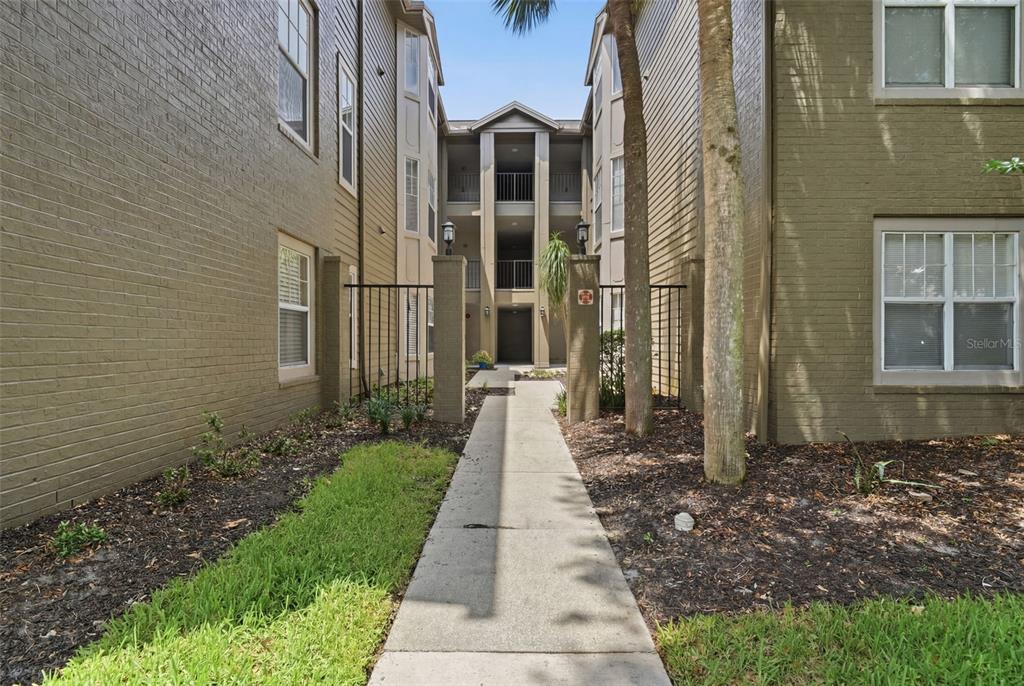 A concrete walkway leads between two multi-story apartment buildings toward a central entrance — 420 SUMMIT RIDGE PLACE UNIT 300, LONGWOOD, FL