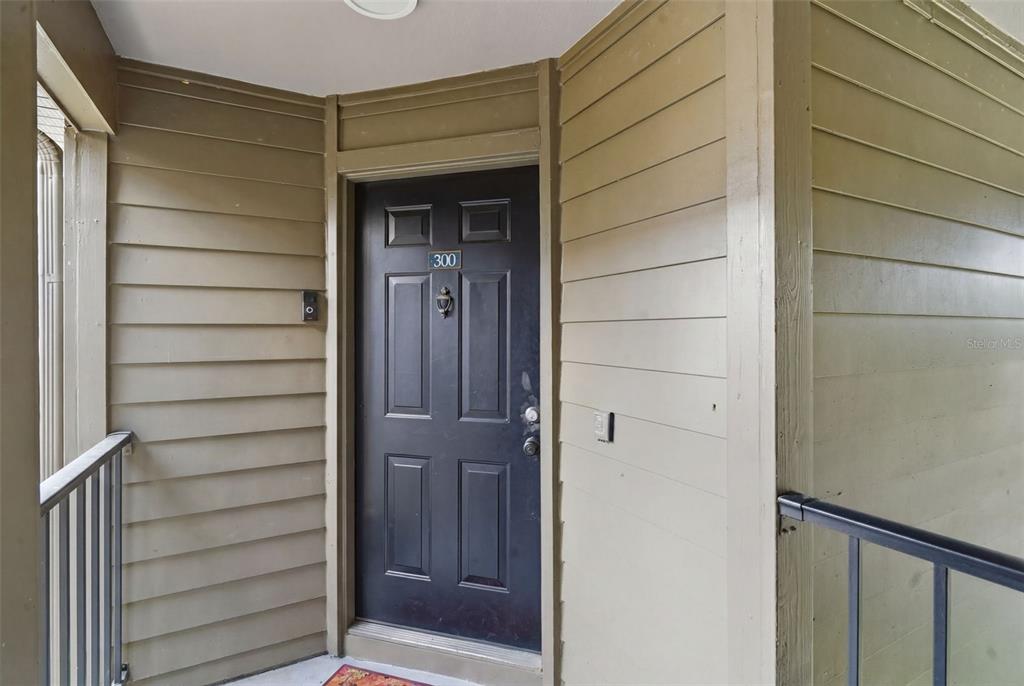 A black front door with the number 300 is set within tan horizontal siding — 420 SUMMIT RIDGE PLACE UNIT 300, LONGWOOD, FL