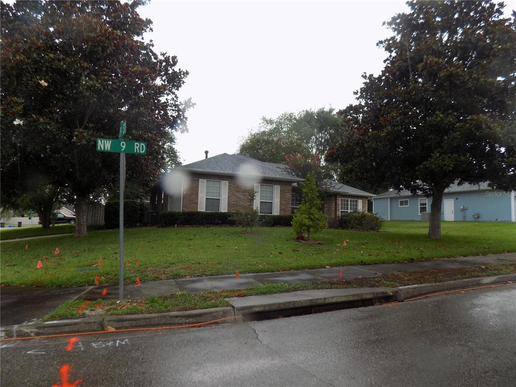 A single-story brick house sits on a corner lot with a street sign nearby — 11903 NW 9TH ROAD, GAINESVILLE, FL