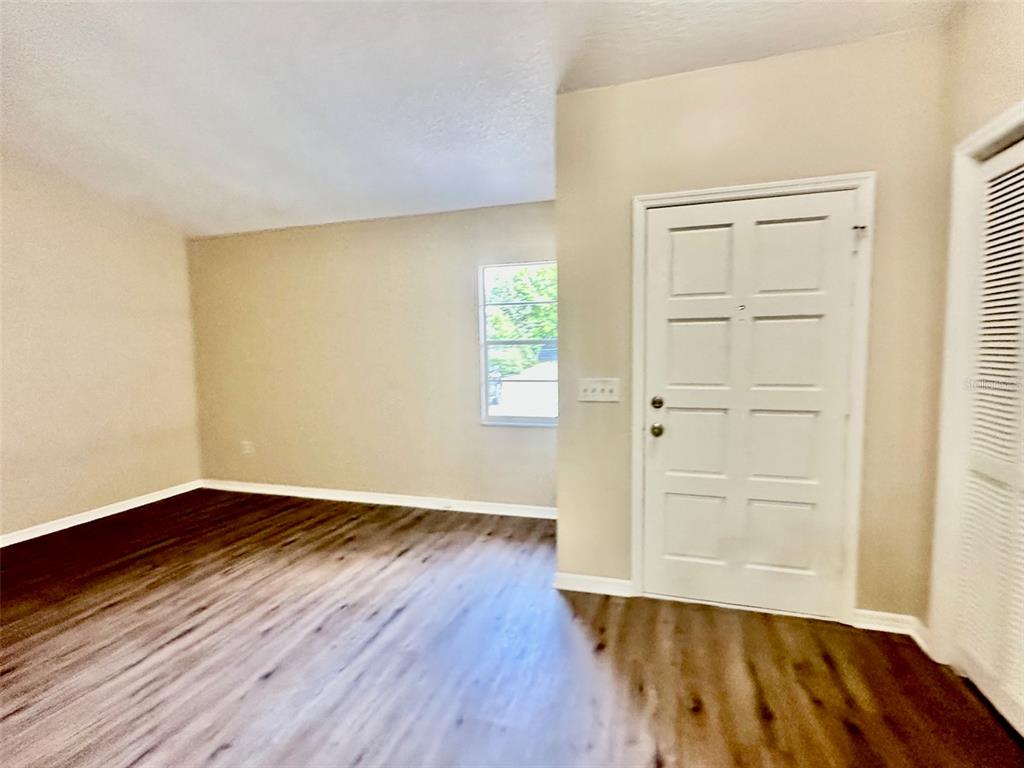 An empty room features wood-look flooring, beige walls, a window, and a white entry door — 15082 SW 38TH CIRCLE, OCALA, FL