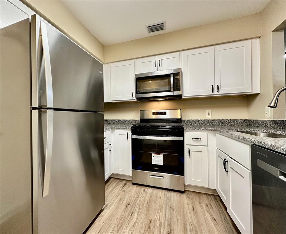 A kitchen features stainless steel appliances, white cabinets, and granite countertops over wood-look flooring — 15082 SW 38TH CIRCLE, OCALA, FL