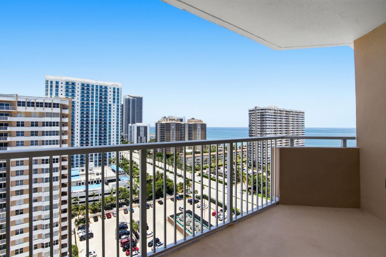 A balcony with a metal railing overlooks a parking lot, surrounding high-rise buildings, and ocean — 1985 S Ocean Drive # 17d, Hallandale Beach FL 33009, HALLANDALE BEACH, FL