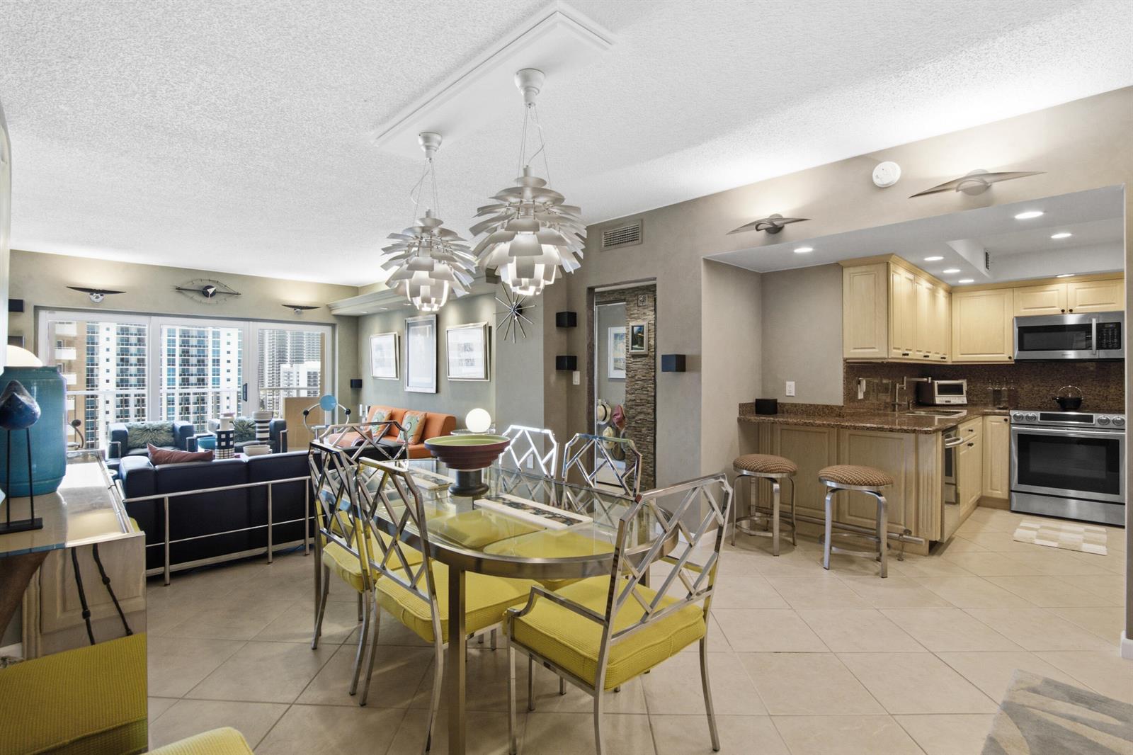 An open-concept dining area with a glass table and kitchen with light wood cabinets — 1985 S Ocean Drive # 17d, Hallandale Beach FL 33009, HALLANDALE BEACH, FL