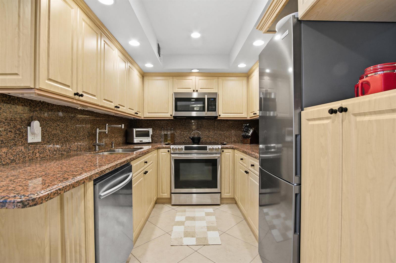 A galley kitchen features light wood cabinets, granite countertops, and stainless steel appliances — 1985 S Ocean Drive # 17d, Hallandale Beach FL 33009, HALLANDALE BEACH, FL