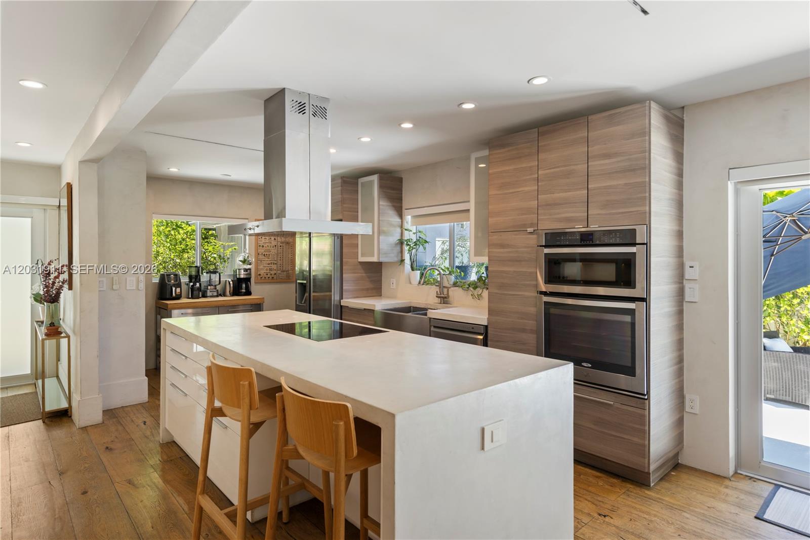 A modern kitchen features a large concrete island, wood-grain cabinetry, and stainless steel appliances — 651 NE 52nd Ter, Miami FL 33137, MIAMI, FL