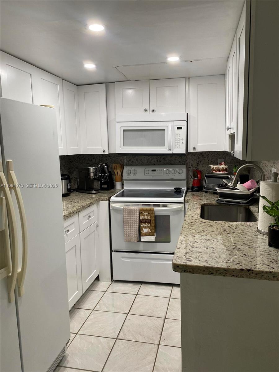 A small kitchen features white cabinets, granite countertops, and white appliances — 9405 W Flagler St # D105, Miami FL 33174, MIAMI, FL