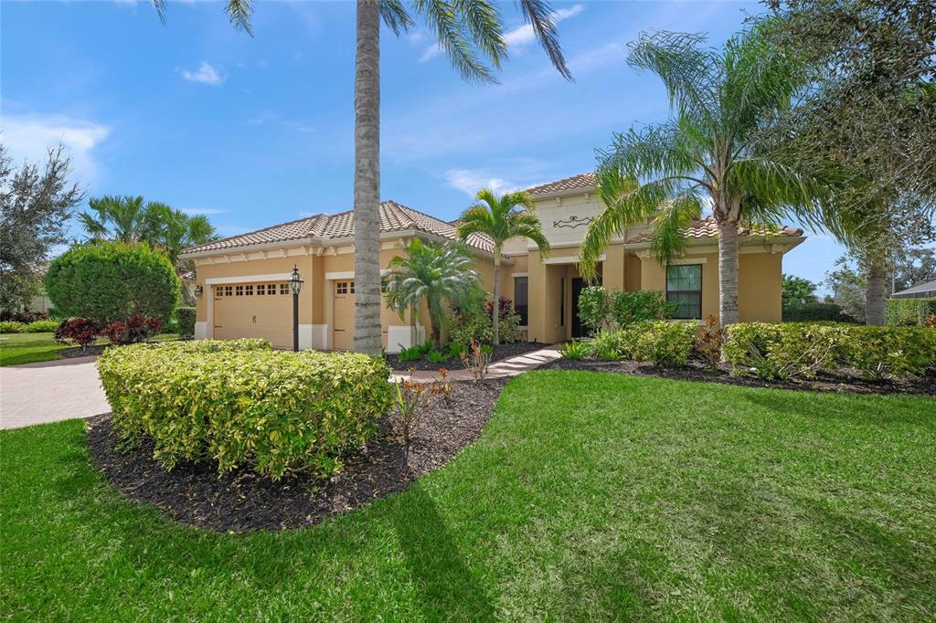 A single-story tan stucco house with a tile roof, palm trees, and a landscaped yard — 7809 PASSIONFLOWER DRIVE, SARASOTA, FL