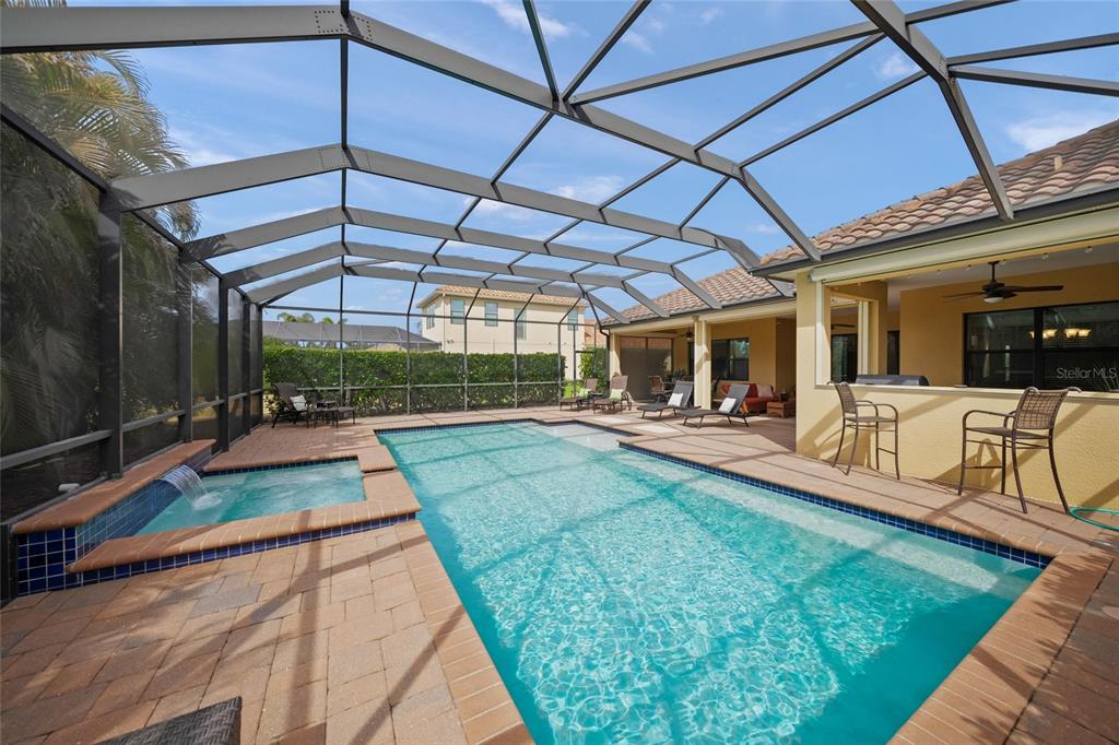 A swimming pool and spa are enclosed within a screened lanai next to a house — 7809 PASSIONFLOWER DRIVE, SARASOTA, FL