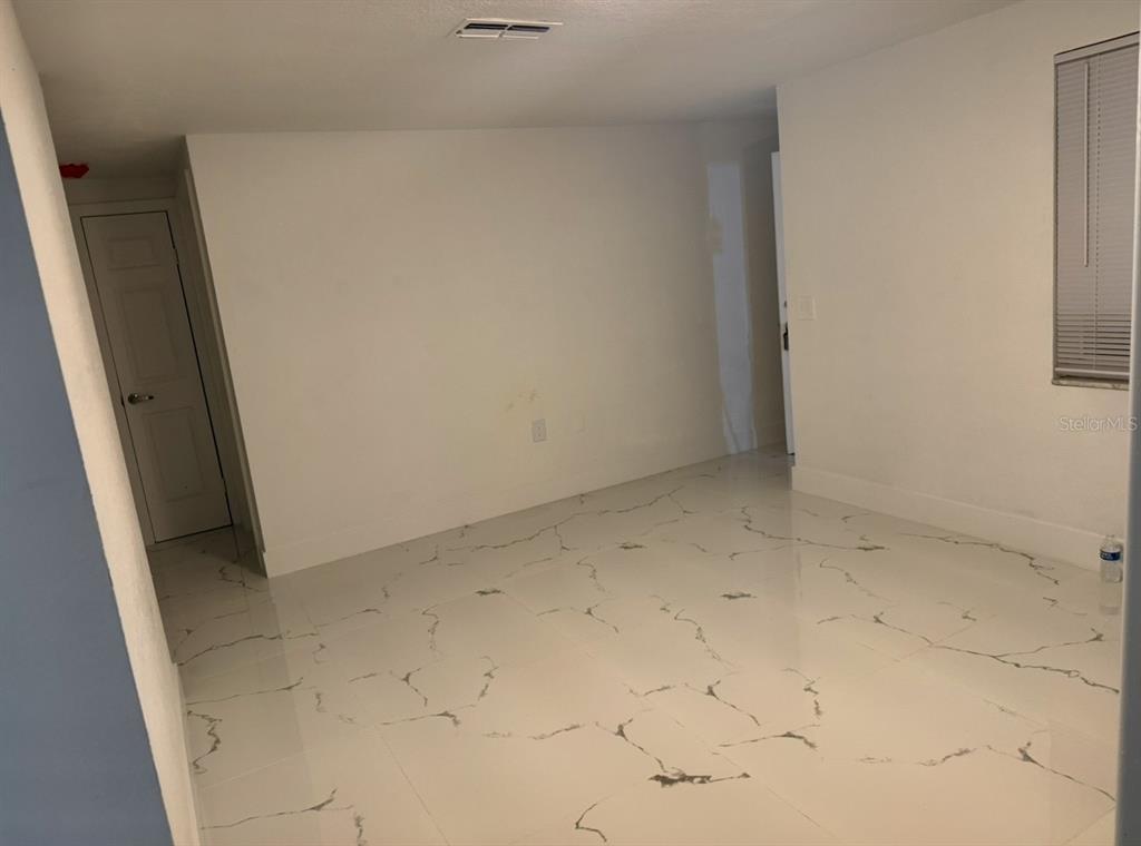 An empty room features white marble-look tile flooring, white walls, and two closed doors — 4453 TERRY LOOP, NEW PORT RICHEY, FL