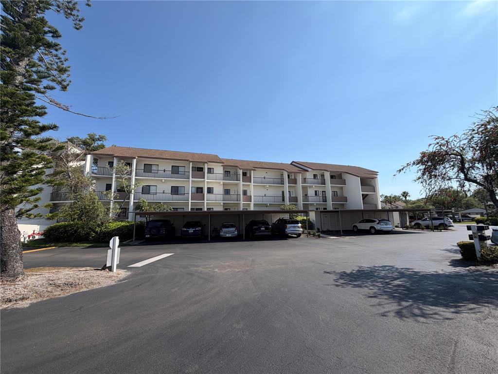 A multi-story apartment building features covered parking spaces in front under a clear blue sky — 832 BIRD BAY WAY UNIT 113, VENICE, FL