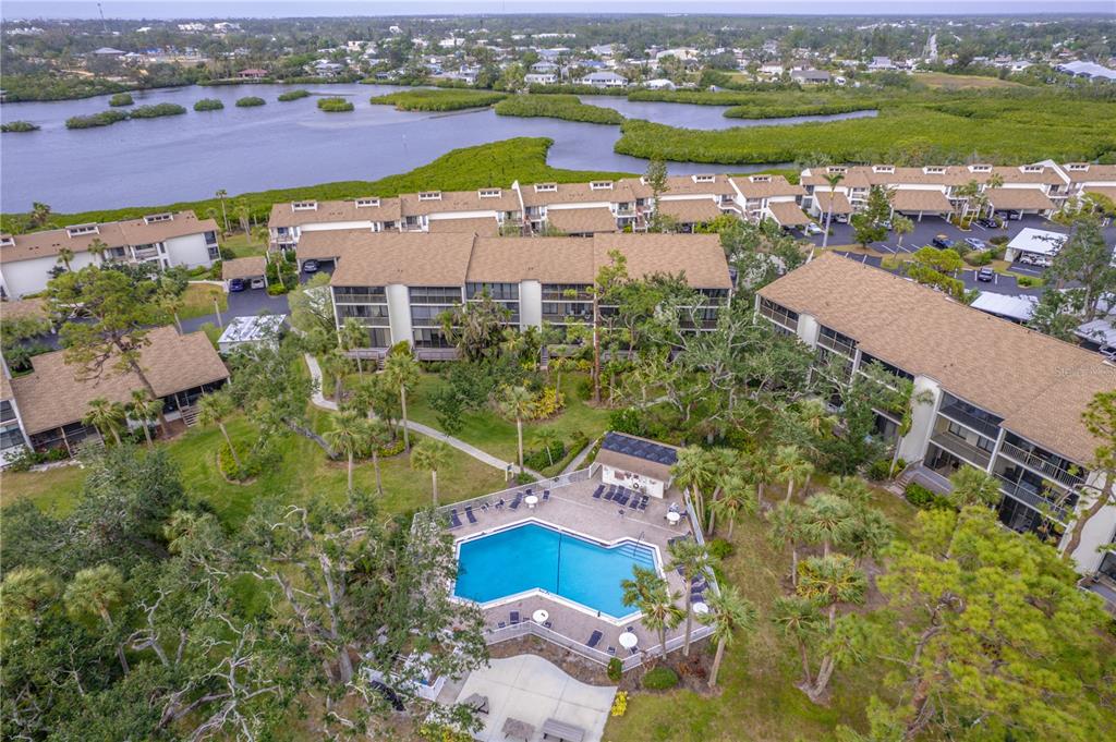 An aerial view shows a swimming pool surrounded by multi-story apartment buildings and trees — 832 BIRD BAY WAY UNIT 113, VENICE, FL