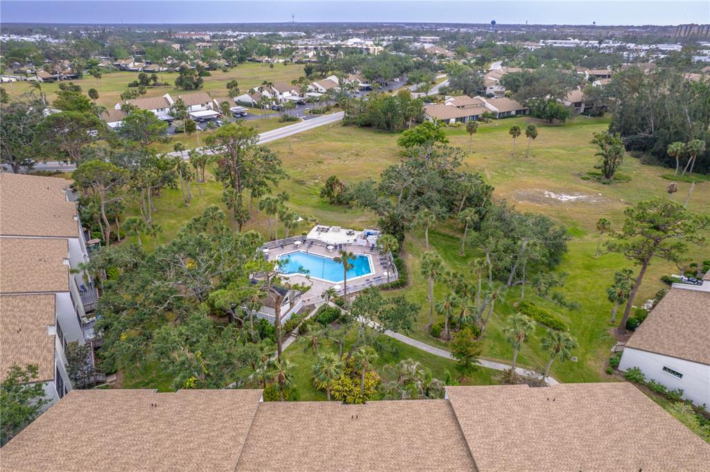 An aerial view shows a swimming pool surrounded by trees and residential buildings — 832 BIRD BAY WAY UNIT 113, VENICE, FL