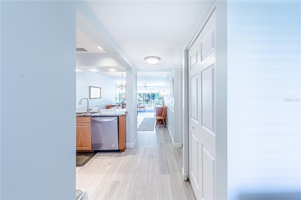 A hallway with light wood-look flooring leads past a kitchen into a living area — 832 BIRD BAY WAY UNIT 113, VENICE, FL