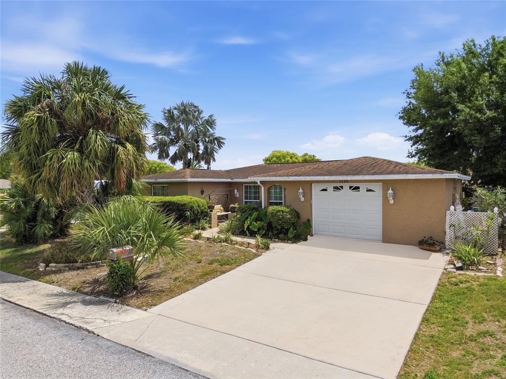 A single-story house with a tan stucco exterior, a white garage door, and palm trees — 7140 ROCKWOOD DRIVE, PORT RICHEY, FL