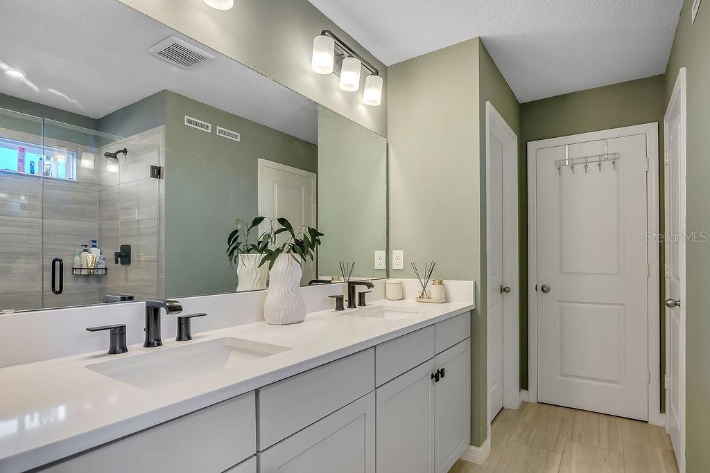 A bathroom features a double vanity with white countertops, gray cabinets, and a large mirror — 1545 LEAF LANE, KISSIMMEE, FL