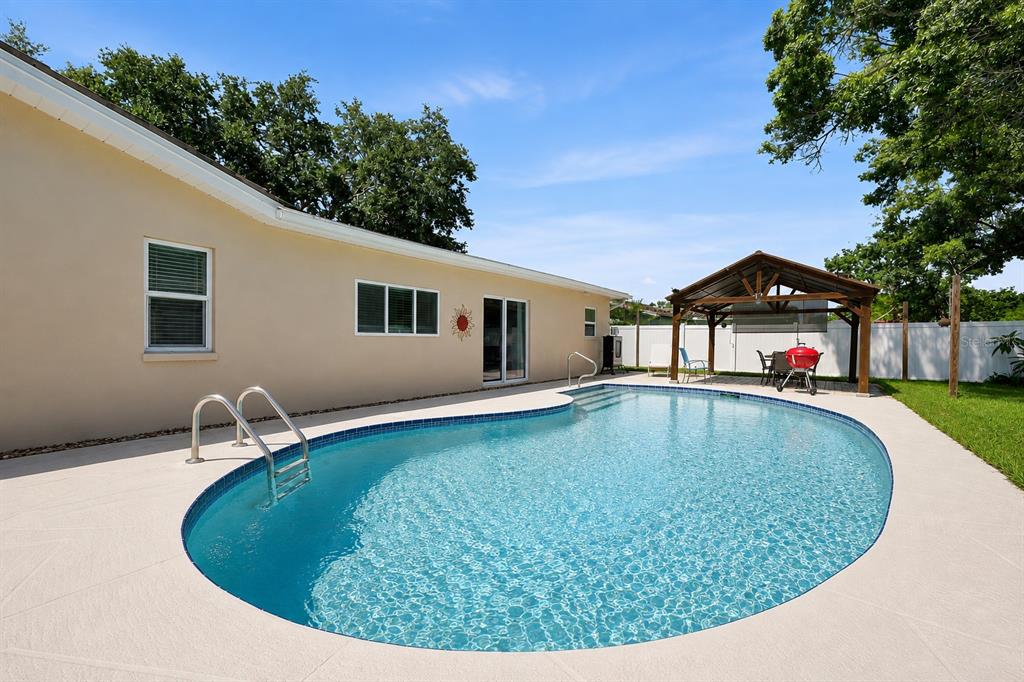 A backyard features a swimming pool with a ladder next to a house and gazebo — 2069 KINGFISHER DRIVE, PALM HARBOR, FL