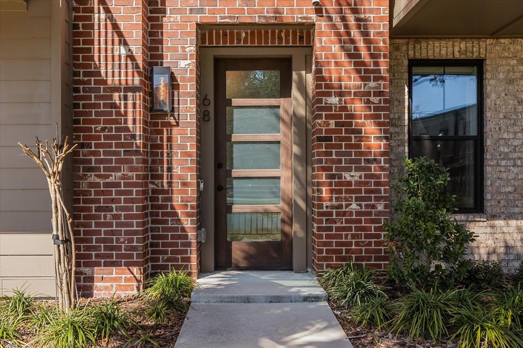 A front entrance with a modern wooden door, frosted glass panels, and red brick siding — 68 N PARK AVENUE, WINTER GARDEN, FL