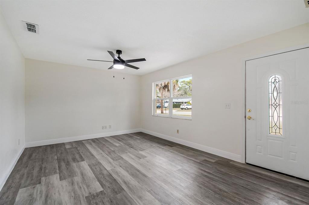 A living room features light walls, gray wood-look flooring, a ceiling fan, and an entry door — 3220 NETHERWOOD DRIVE, WINTER PARK, FL