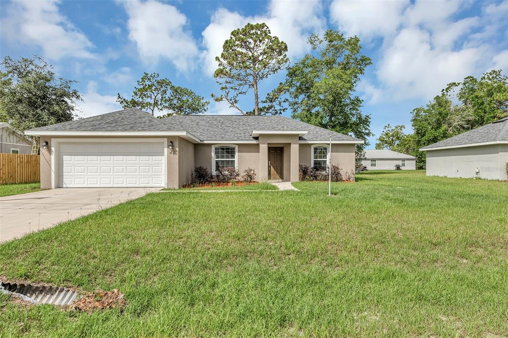 The exterior of a house features a tan stucco wall, a brown front door, and landscaping — 42 WATER TRACK DRIVE, OCALA, FL