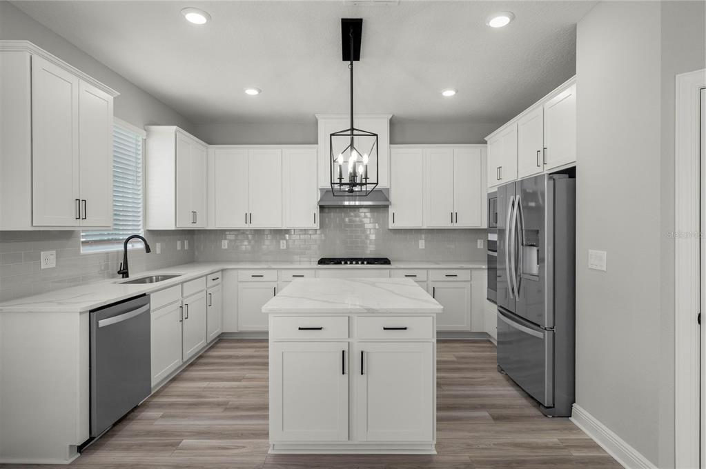 A modern kitchen features white cabinets, a marble-topped island, stainless steel appliances, and wood flooring — 7891 SOMERSWORTH DRIVE, KISSIMMEE, FL