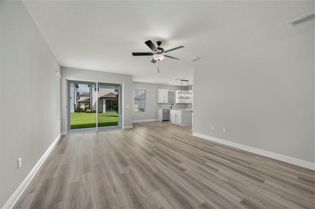 An open-concept living area with light gray walls, wood-look flooring, and a view of the kitchen — 7891 SOMERSWORTH DRIVE, KISSIMMEE, FL