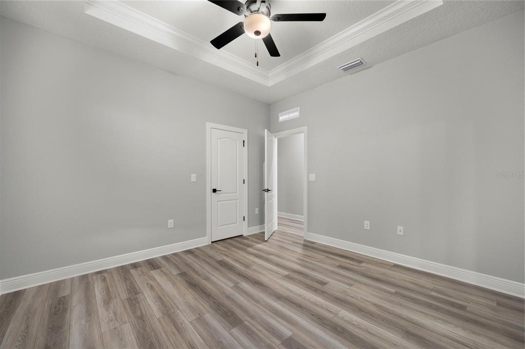 A bedroom with gray walls, wood-look flooring, a tray ceiling, and two white doors — 7891 SOMERSWORTH DRIVE, KISSIMMEE, FL