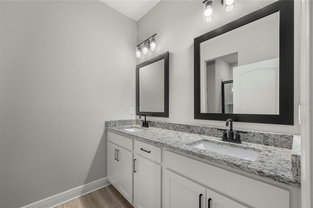A bathroom features a double vanity with white cabinets, granite countertops, and two black-framed mirrors — 7891 SOMERSWORTH DRIVE, KISSIMMEE, FL