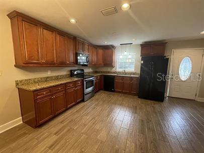 A kitchen features wood cabinets, granite countertops, stainless steel appliances, and wood-look tile flooring — 12 BUNKER VIEW PLACE, PALM COAST, FL