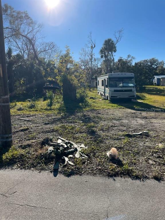 A vacant lot features a parked recreational vehicle, scattered debris, and several trees under sunlight — E SPRUCE STREET, DAYTONA BEACH, FL
