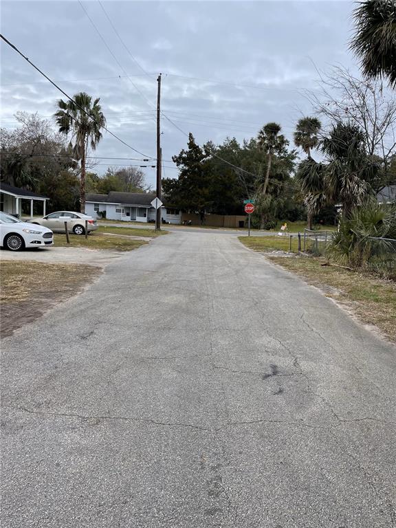 A paved residential street leads toward a stop sign near several houses and palm trees — E SPRUCE STREET, DAYTONA BEACH, FL