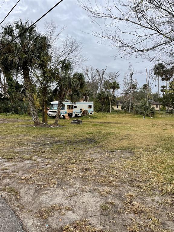 A vacant, grassy lot features a damaged motorhome parked near several palm trees — E SPRUCE STREET, DAYTONA BEACH, FL