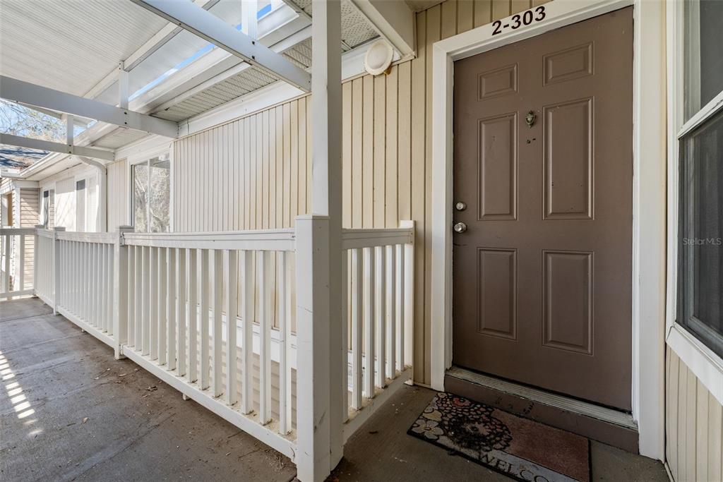 A brown front door with the number 2-303 above it sits on a covered porch — 4000 SW 23RD STREET UNIT 2-303, GAINESVILLE, FL