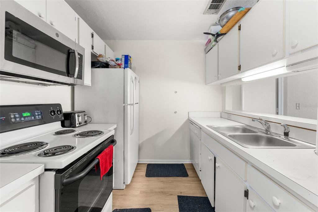 A galley kitchen features white cabinets, a black electric stove, and a stainless steel sink — 4000 SW 23RD STREET UNIT 2-303, GAINESVILLE, FL