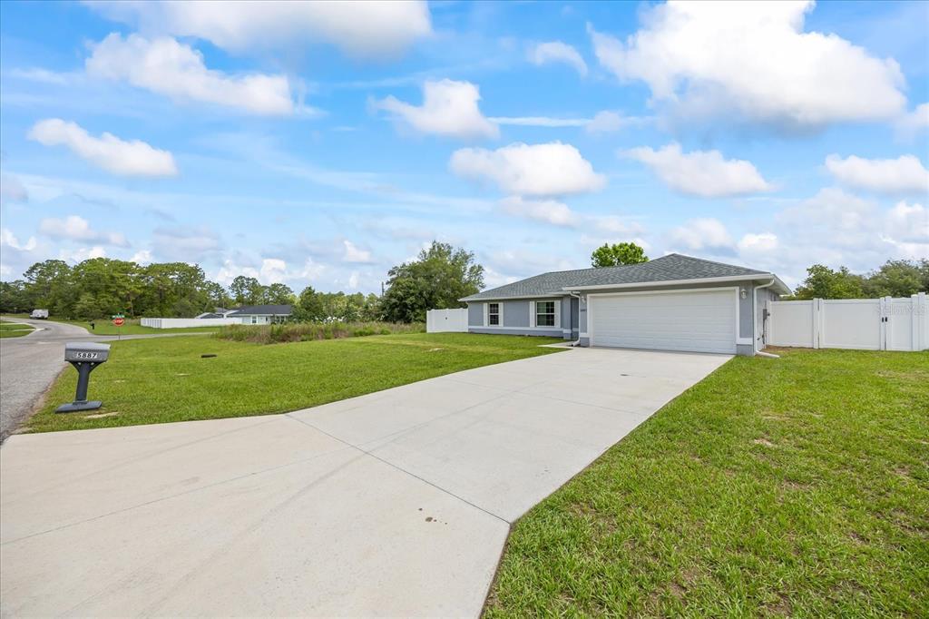 A single-story house with a white garage door and a concrete driveway under a blue sky — 5887 SW 154TH LANE ROAD, OCALA, FL