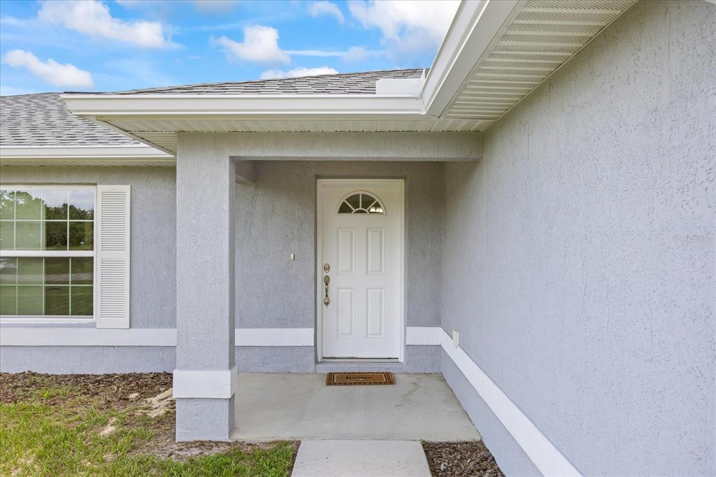 A gray stucco house exterior features a white front door and a covered concrete porch — 5887 SW 154TH LANE ROAD, OCALA, FL