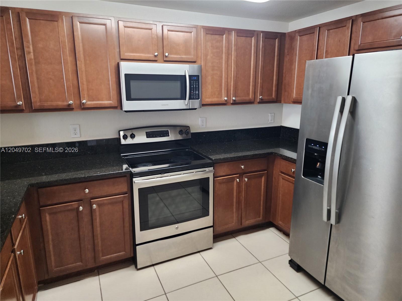 A kitchen features wood cabinets, stainless steel appliances, and dark countertops over tiled flooring — 8960 NW 97th Ave # 102, Doral FL 33178, DORAL, FL