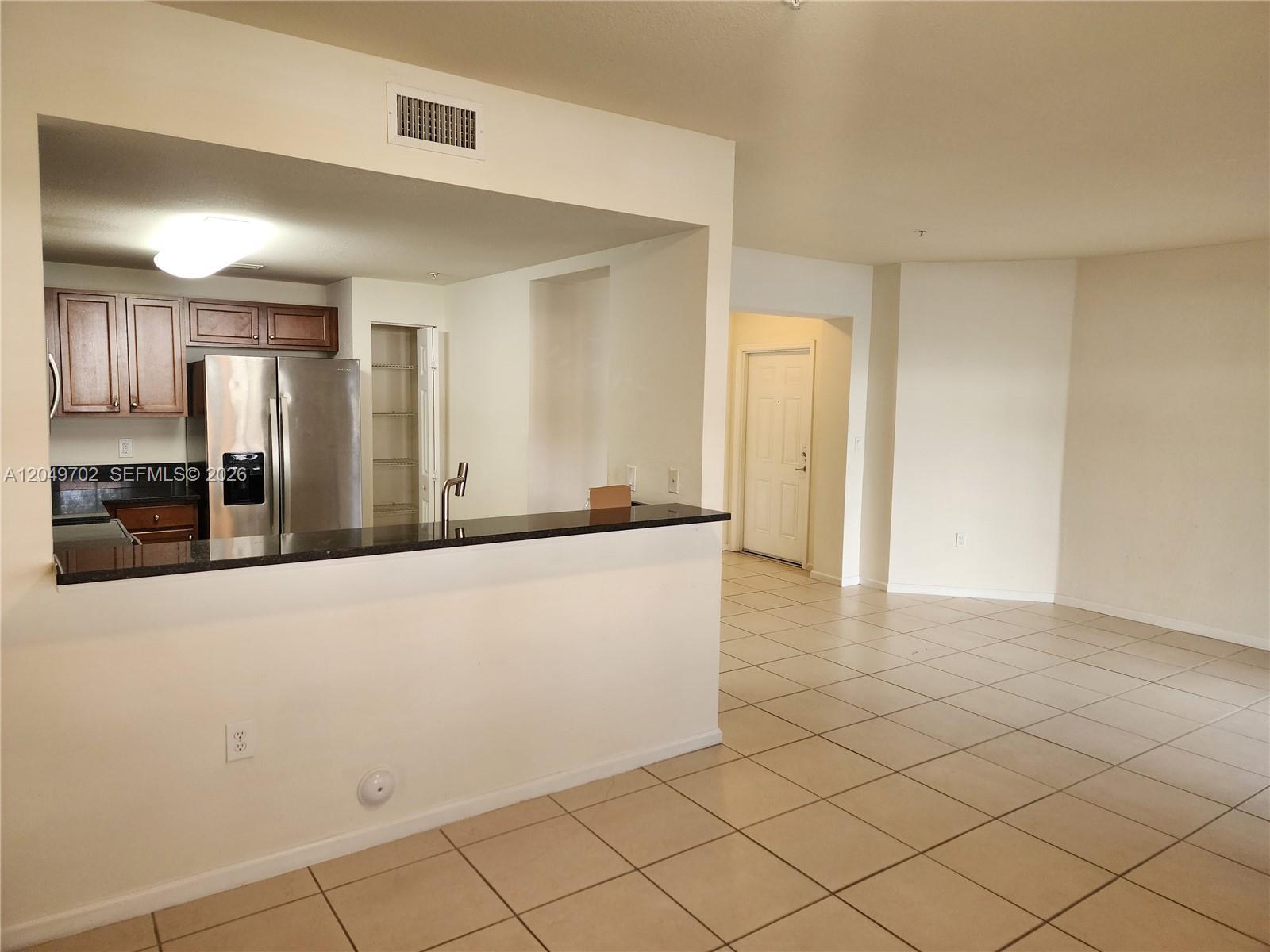 A kitchen with dark wood cabinets and a breakfast bar overlooks a tiled living area — 8960 NW 97th Ave # 102, Doral FL 33178, DORAL, FL