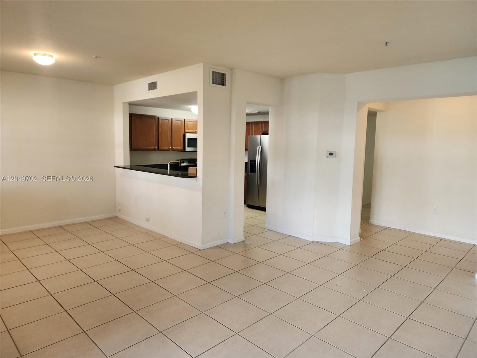 An open-concept living area features light-colored tile flooring and a kitchen with dark countertops — 8960 NW 97th Ave # 102, Doral FL 33178, DORAL, FL