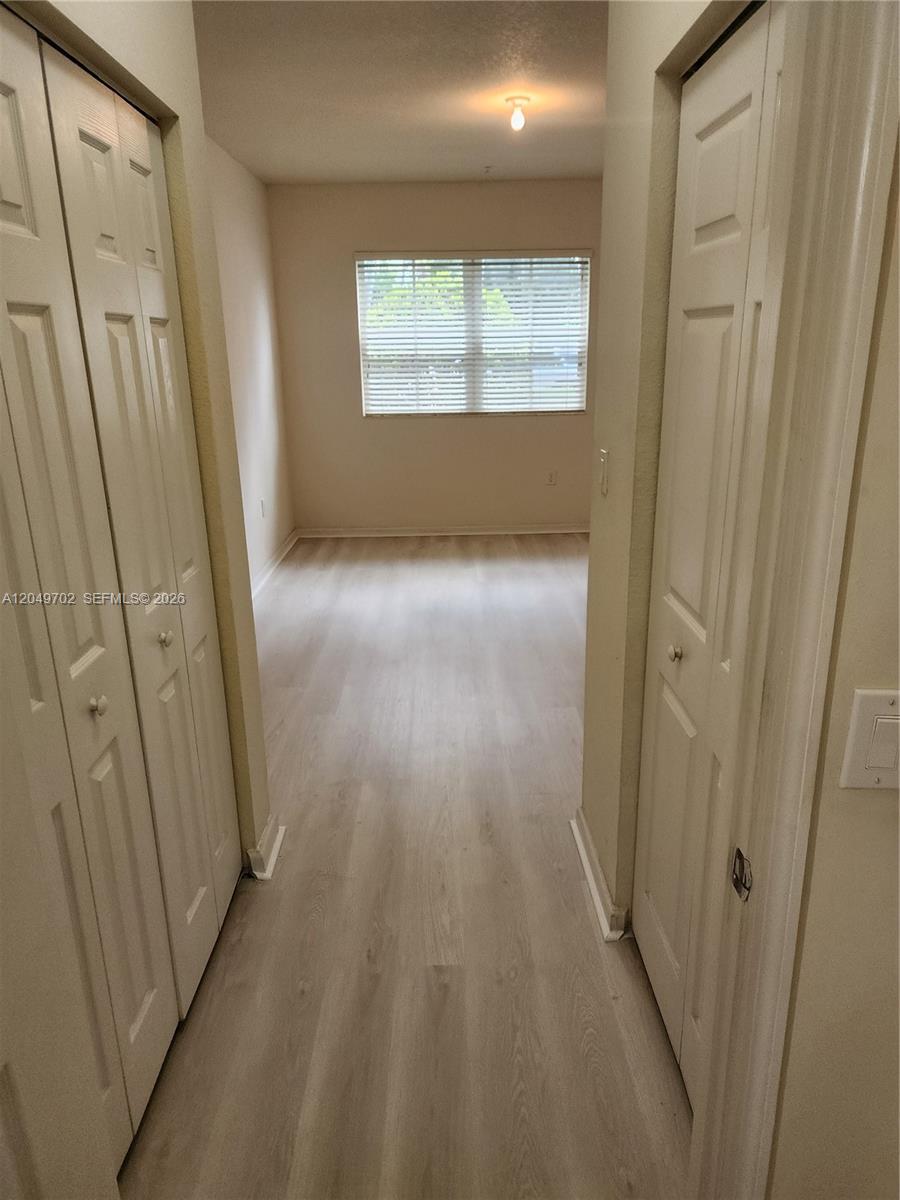 A hallway with light wood-look flooring leads to a bedroom with a window — 8960 NW 97th Ave # 102, Doral FL 33178, DORAL, FL