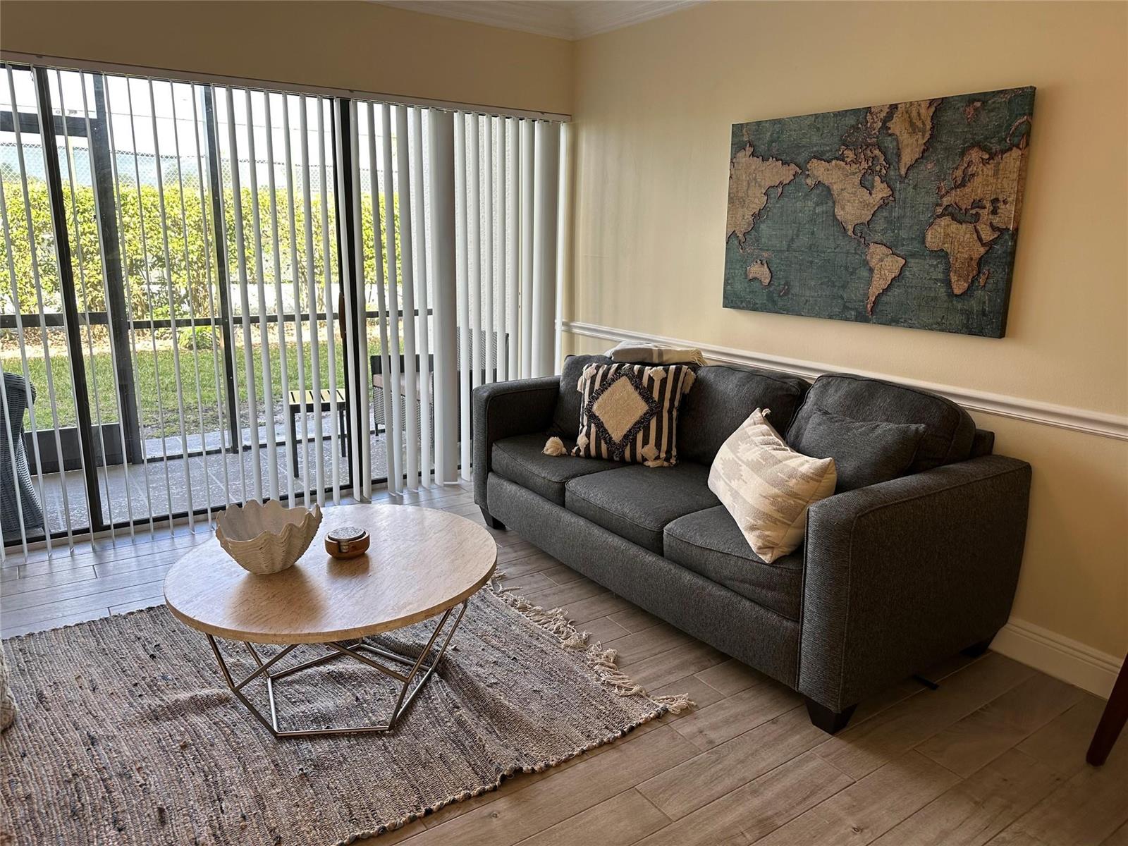 A living room features a gray sofa, a round coffee table, and a world map — 1605 US Highway 1 V-4 # 104, Jupiter FL 33477, JUPITER, FL