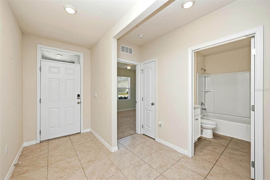 An entryway with tile flooring, a white front door, a bathroom, and a bedroom doorway — 2725 DUMONT LANE, TAVARES, FL